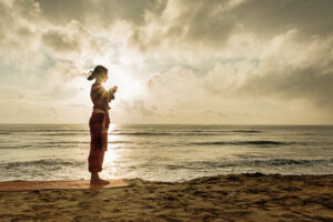 A lady performing surya namaskar on a beach at sunrise