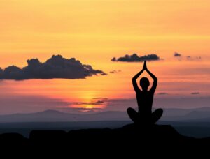 A lady performing a sitting yoga pose on a mountain against a sunrise, silhouette